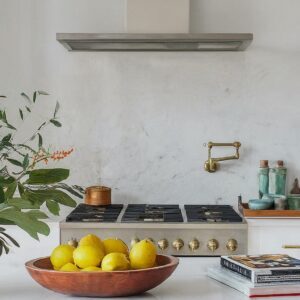A bright and inviting all white kitchen with a rustic touch, featuring a bowl of lemons, green plants, and decorative item