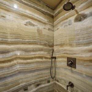 A luxurious shower with onyx walls featuring natural, earthy tones and horizontal veining patterns.